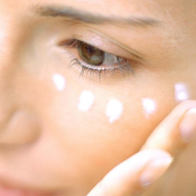 Mulher a aplicar creme branco sob o olho