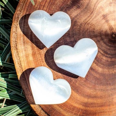 Três corações brancos translúcidos de selenita sobre madeira redonda com folhas verdes ao redor