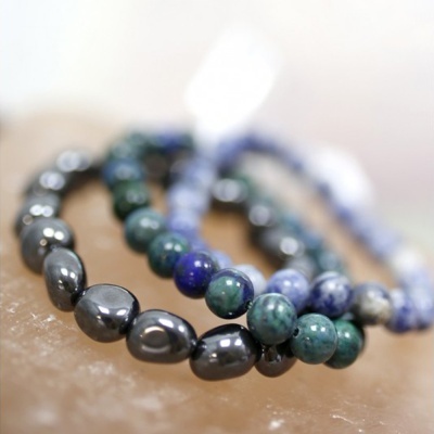 Três pulseiras com contas azuis, verdes e prateadas sobre superfície rosa