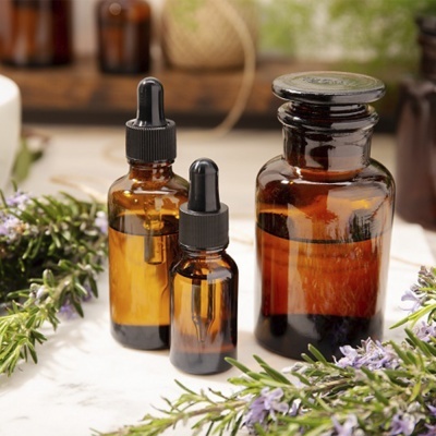 Três frascos de vidro âmbar com conta-gotas e flores lilases ao redor.