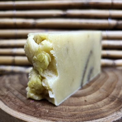 Sabonete artesanal bege com pedaços sólidos em base de madeira e fundo de bambu