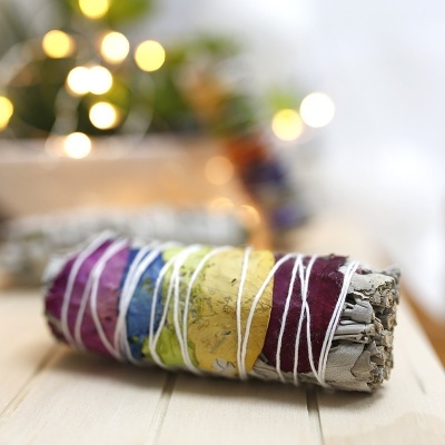 Feixe de sálvia branca com folhas coloridas enrolado em fio branco sobre madeira