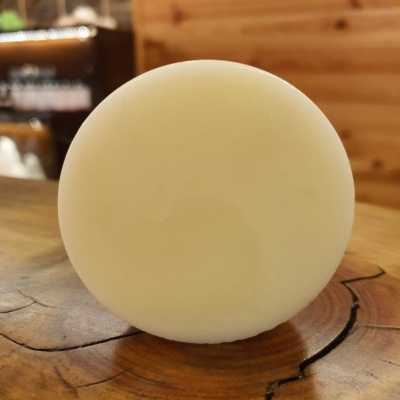 Sabonete redondo branco sobre madeira com parede de madeira e prateleiras ao fundo