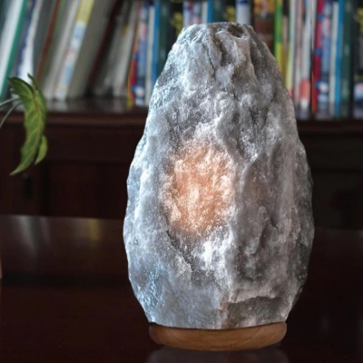 Luminária de sal cinzenta com base de madeira sobre mesa escura em frente a estante de livros