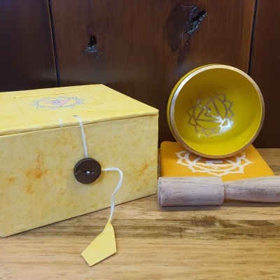 Conjunto de caixa amarela, tigela amarela com símbolo branco, suporte com estampa branca e bastão de madeira numa superfície de madeira.