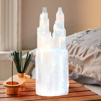 Escultura branca cristalina em formato de torre sobre mesa de madeira com suporte de incenso ao lado