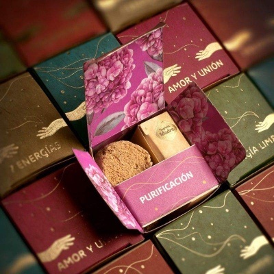 Caixa de sabonetes florais com texto PURIFICACIÓN aberta, rodeada por outras caixas fechadas com diferentes textos e cores.