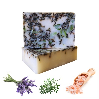 Barras de sabão artesanal com ingredientes naturais, ramos de lavanda, folhas verdes e sal grosso numa colher de madeira