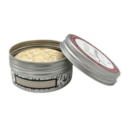 Lata metálica prateada aberta com shampoo sólido bege e rótulo com texto