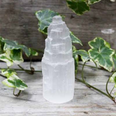 Escultura de cristal branco translúcido em forma de torre, com folhas verdes ao fundo