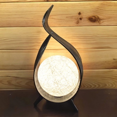 Luminária de mesa com estrutura metálica preta e esfera branca iluminada sobre superfície escura com fundo de madeira