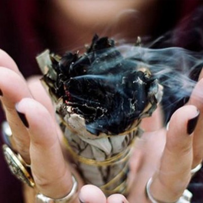 Feixe de sálvia branca a arder nas mãos de pessoa com unhas pretas e anéis prateados