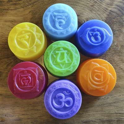 Sabonetes coloridos redondos com símbolos chakras gravados, dispostos sobre madeira.