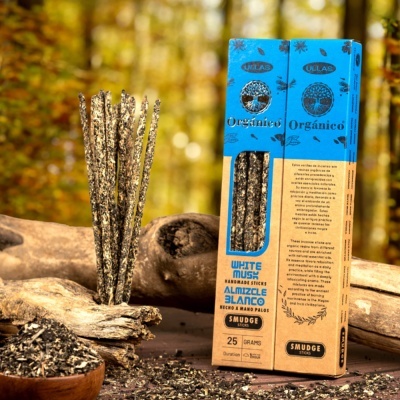 Incensos artesanais White Musk Almizcle Blanco em embalagem azul e castanho com sticks e ervas secas sobre troncos numa cena natural.