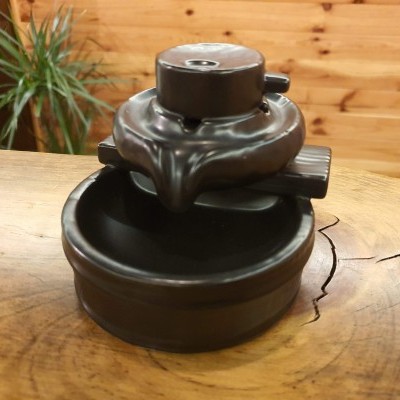 Fonte decorativa de cerâmica preta em mesa de madeira com planta ao fundo