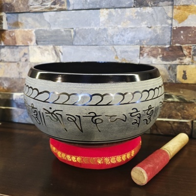 Tigela tibetana prateada com inscriçõs negras e bastão vermelho sobre almofada vermelha