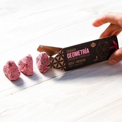 Embalagem preta de sahumerio triangular com três cones cor-de-rosa ao lado sobre superfície clara