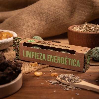 Caixa de produto com texto LIMPIEZA ENERGÉTICA sobre mesa de madeira com ervas e resina