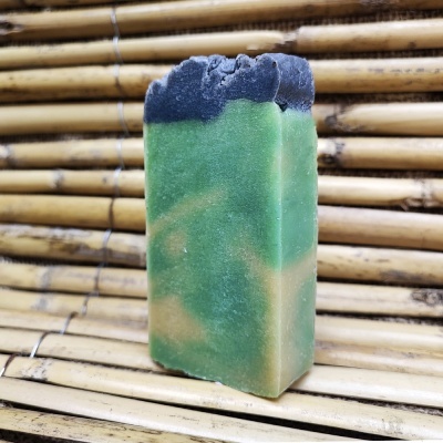 Sabonete artesanal verde com topo preto sobre superfície de bambu
