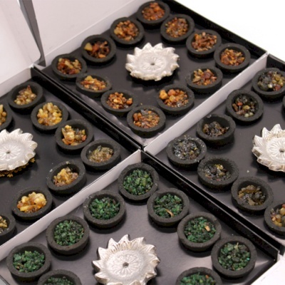 Caixas com pequenos recipientes redondos contendo pedras coloridas e um objeto decorativo prata no centro