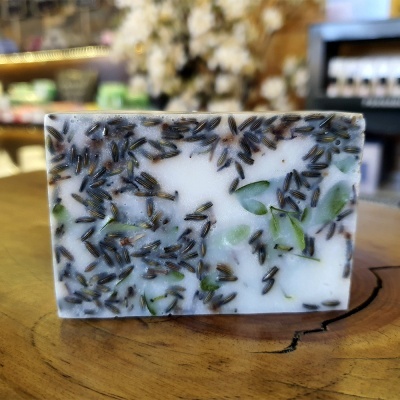 Sabonete artesanal branco com folhas verdes e flores roxas embutidas sobre madeira