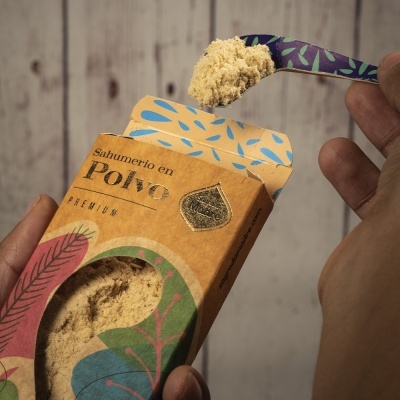 Caixa de sabão em pó premium com design colorido e pó amarelo claro sendo retirado com colher decorada