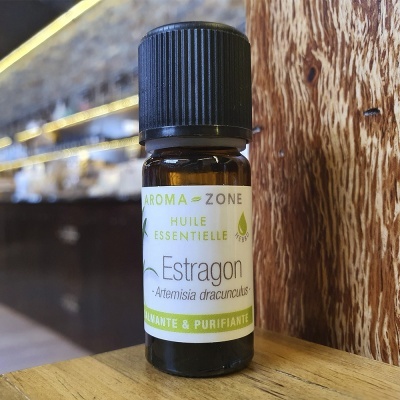 Frasco pequeno de óleo essencial de estragão com tampa preta em superfície de madeira