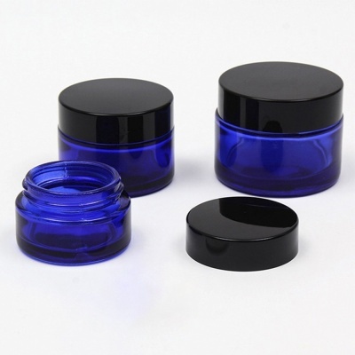 Três frascos pequenos de vidro azul com tampas pretas, um aberto
