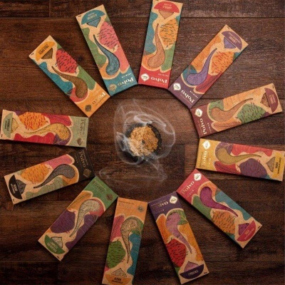 Doze caixas coloridas de incenso dispostas em círculo com incenso queimado ao centro.