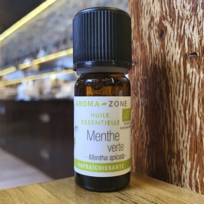 Frasco pequeno de óleo essencial de menta verde com rótulo branco e verde sobre madeira