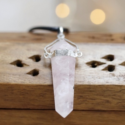 Colar com pendente de pedra rosa facetada e cordão preto sobre madeira