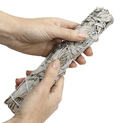 Mãos segurando feixe de folhas secas amarradas com fio branco.