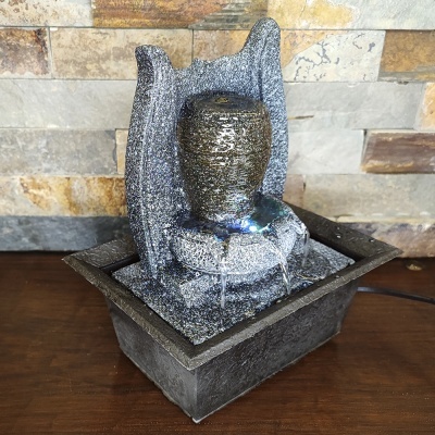 Fonte decorativa cinzenta texturizada com vaso e base quadrada preta sobre mesa de madeira