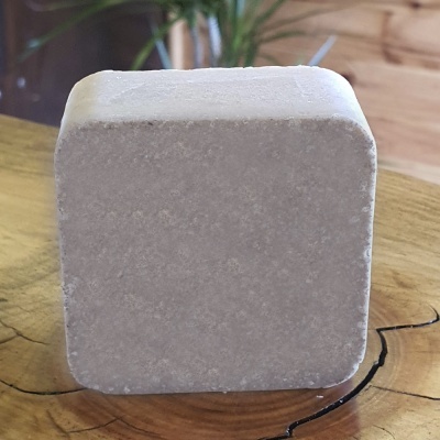 Bloco quadrado cinza claro com textura porosa sobre madeira