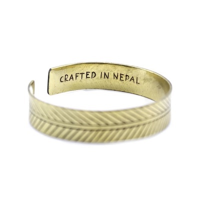 Pulseira dourada aberta com padrão diagonal e inscrição CRAFTED IN NEPAL no interior