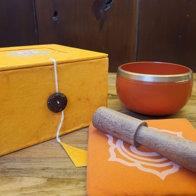 Conjunto com taça de metal ferrugem, almofada laranja, malho de madeira e caixa amarela sobre mesa de madeira