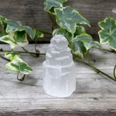 Cristal branco translúcido em formato piramidal sobre superfície de madeira com folhas verdes