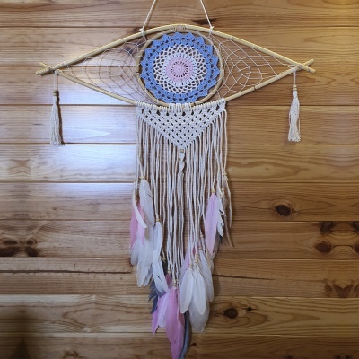 Apanhador de sonhos com cordas, penas e padrão em croché, pendurado em parede de madeira.