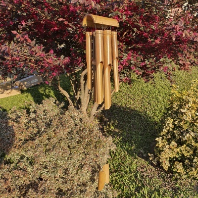 Sino dos ventos de bambu pendurado em arbusto com folhas vermelhas num jardim