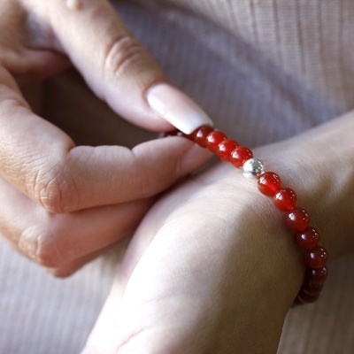 Pulseira de contas vermelhas com uma conta prateada num pulso feminino