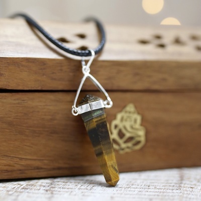 Colar com pendente facetado de pedra castanha e amarela em cordão preto sobre caixa de madeira