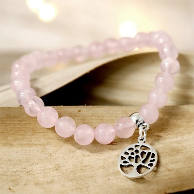 Pulseira com contas rosas de pedra e pendente de árvore prateado sobre madeira clara.