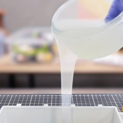 Mão com luva a despejar líquido translúcido para molde branco numa superfície de corte