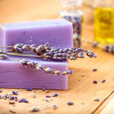 Sabonetes roxos decorados com lavanda sobre madeira com frascos ao fundo