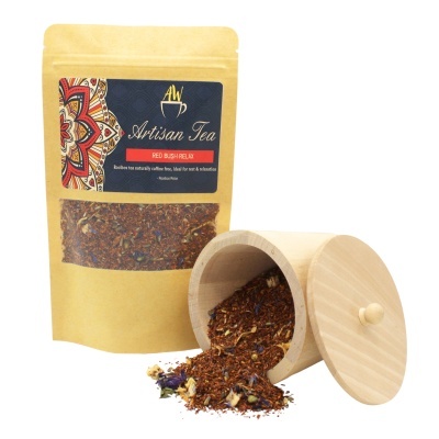 Pacote dourado e preto de chá Artisan Tea Red Bush Relax com recipiente de madeira claro e chá derramado