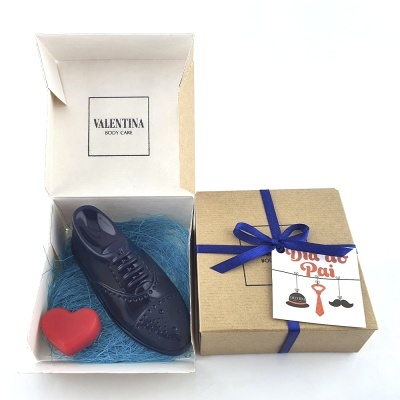 Caixa aberta com sapato feminino de chocolate escuro e coração vermelho, ao lado caixa fechada castanha com fita azul e cartão pai