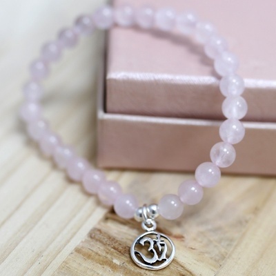 Pulseira de contas cor-de-rosa com pingente metálico simbolizando 'Om' junto a caixa rosa
