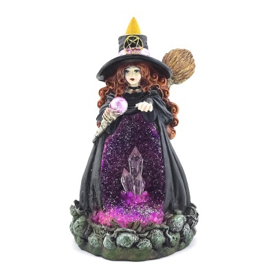 Estátua de bruxa com chapéu preto, vestido roxo brilhante, segurar varinha, base de pedras verdes