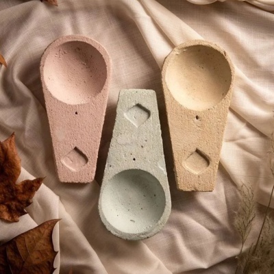 Três incensários de cimento em tons pastéis sobre tecido bege