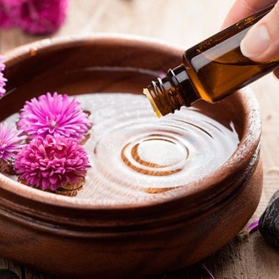 Frasco de vidro castanho a verter líquido numa tigela de barro com flores cor-de-rosa e pedras pretas.